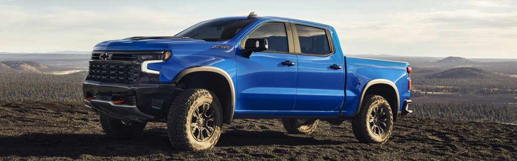 Blue Chevrolet Silverado 1500 pickup truck on rugged terrain with a scenic mountain backdrop
