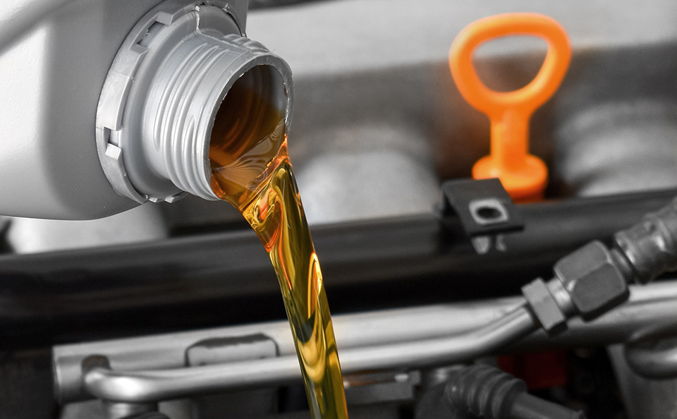 Fresh, golden-amber engine oil being poured from a silver container into a car engine.